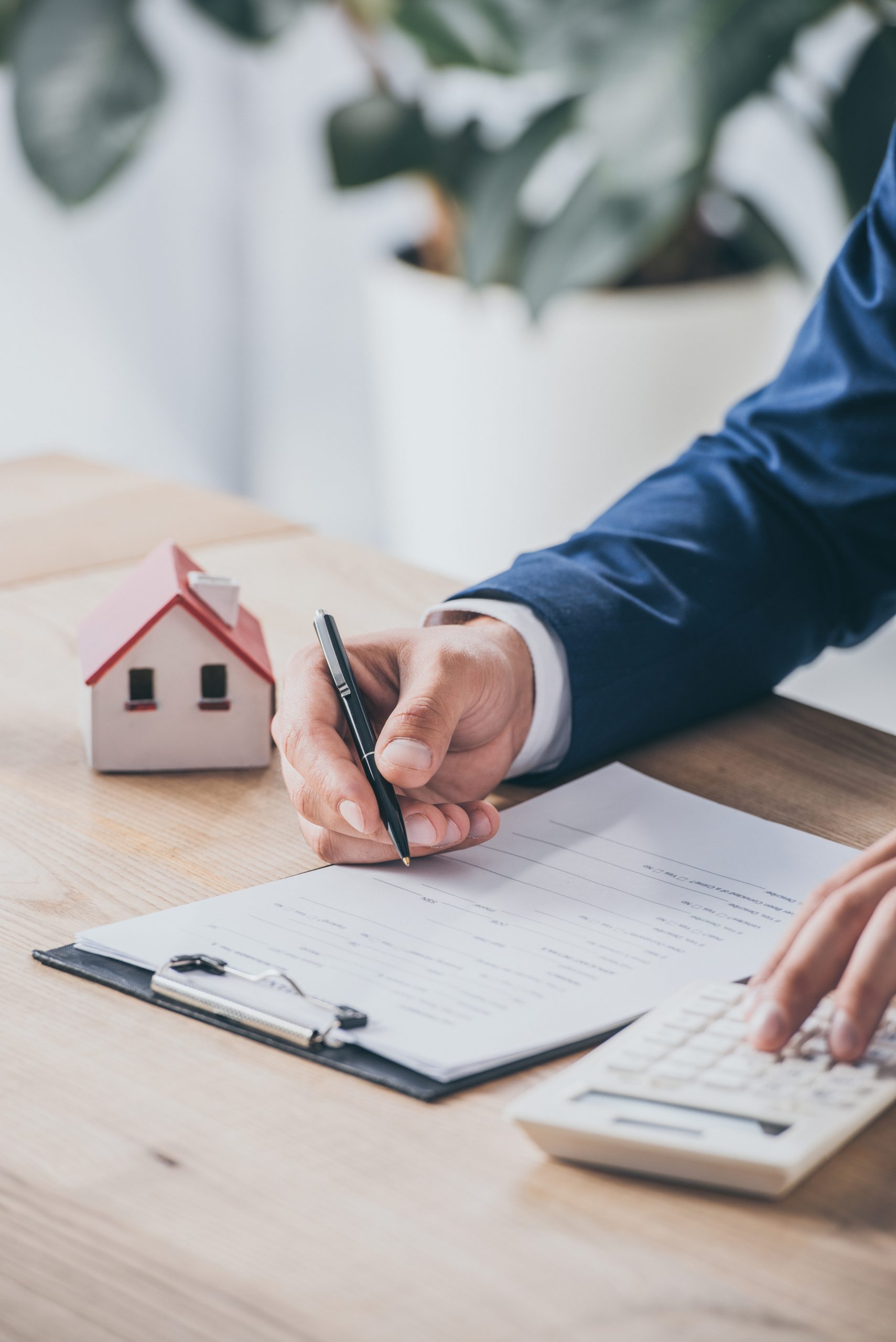 cropped view of businessman using calculator and writing in contract near house model
